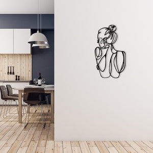 May include: Black metal wall art depicting a line drawing of a woman with her hair in a bun, facing away from the viewer.