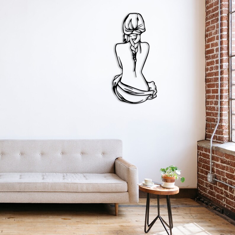 May include: Black metal wall art depicting a woman sitting with her back to the viewer, her hair in a braid. The art is mounted on a white wall.