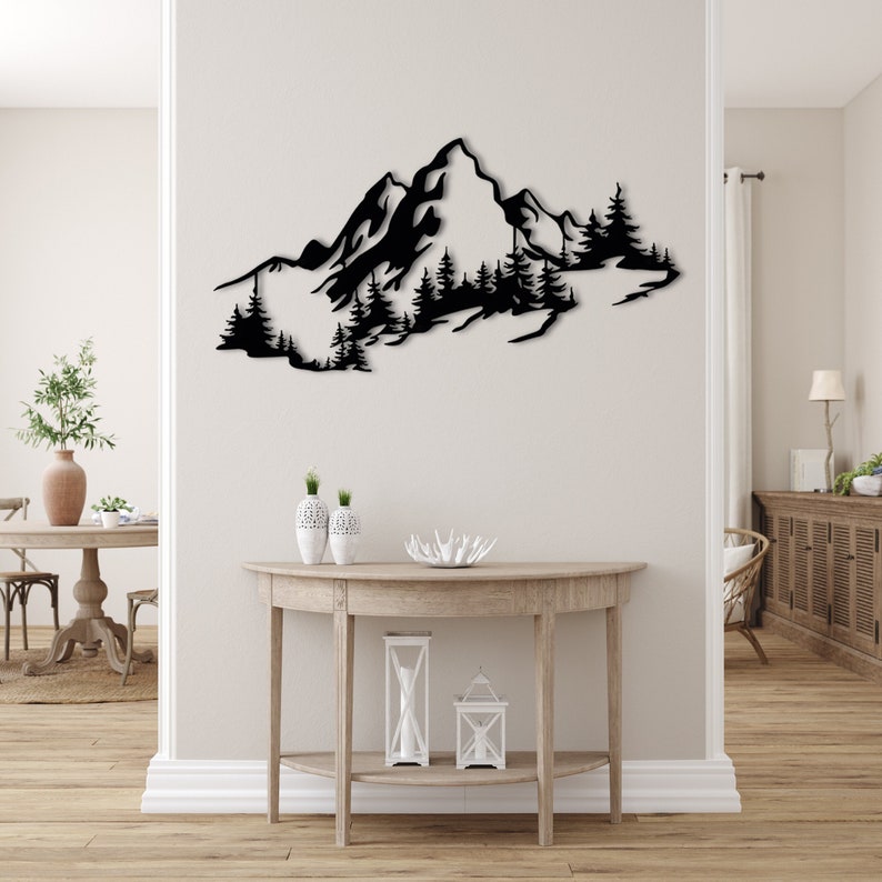 May include: Black metal wall art depicting a mountain range with trees. The art is mounted on a white wall above a wooden console table.