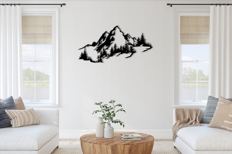 May include: Black metal wall art depicting a mountain range with trees. The art is mounted on a white wall in a living room setting.