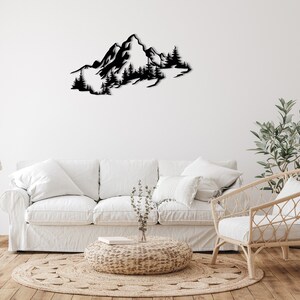 May include: Black metal wall art depicting a mountain range with trees. The art is displayed on a white wall above a white couch and a wicker chair.