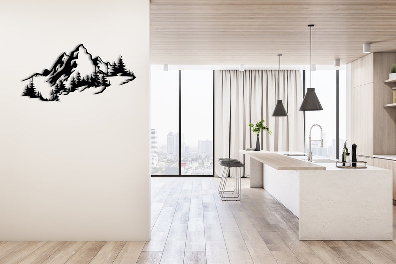 May include: A black metal wall art sculpture depicting a mountain range with trees. The sculpture is mounted on a white wall in a modern kitchen with a white countertop and a large window.