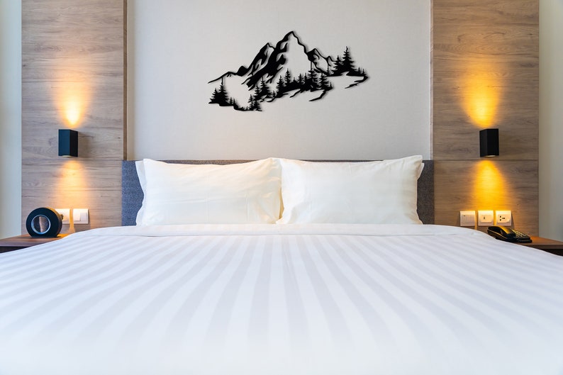 May include: A white bed with a white duvet cover and two white pillows. The bed is in a bedroom with a wooden headboard and a black metal wall sculpture of a mountain range with trees.