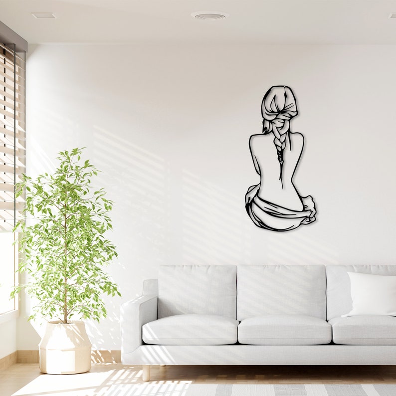 May include: Black metal wall art depicting a woman sitting with her back to the viewer, her hair in a braid. The art is mounted on a white wall in a living room setting.