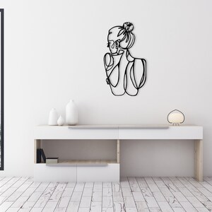 May include: Black metal wall art featuring a line drawing of a woman with her hair in a bun.