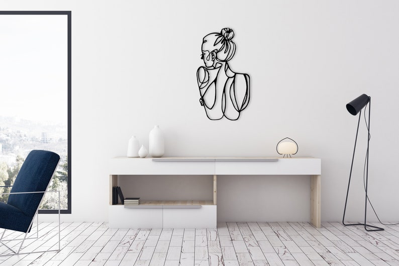 May include: Black metal wall art featuring a line drawing of a woman with her hair in a bun.