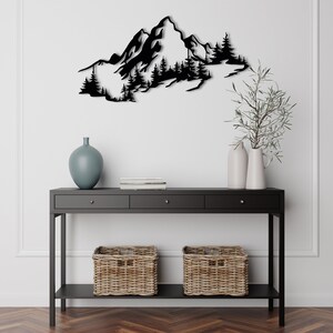 May include: Black metal wall art depicting a mountain range with trees. The art is mounted on a white wall above a black console table with two wicker baskets.