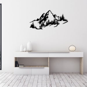 May include: Black metal wall art depicting a mountain range with trees. The art is mounted on a white wall above a white shelf with a lamp and decorative items.