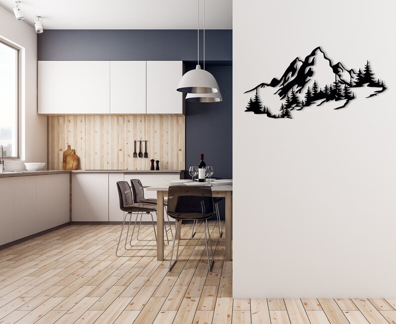 May include: A black metal wall art sculpture depicting a mountain range with trees. The sculpture is mounted on a white wall in a modern kitchen with a wooden floor and a dining table with chairs.