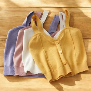 May include: Four sleeveless tops in different colors: purple, pink, white, and yellow. The yellow top has a heart-shaped button closure.