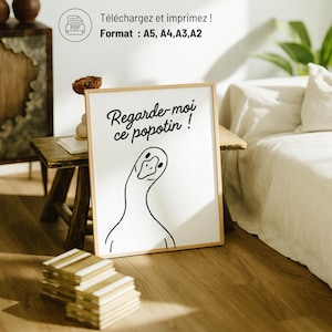K&ouml;nnte beinhalten: Ein gerahmter Druck mit einer minimalistischen Illustration einer Gans und dem Text "Regarde-moi ce popotin!". Der Druck befindet sich in einem Holzrahmen und wird auf einem kleinen Holztisch ausgestellt. Das Bild enth&auml;lt auch den Text "T&eacute;l&eacute;chargez et imprimez! Format: A5, A4, A3, A2".