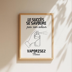 K&ouml;nnte beinhalten: Ein gerahmter Druck mit wei&szlig;em Hintergrund und schwarzem Text. Der Text lautet "LE SUCC&Egrave;S SE SAVOURE pas son odeur" und "VAPORISEZ Merci". Eine Hand wird beim Spr&uuml;hen einer Flasche dargestellt. Der Rahmen ist hellbraun.