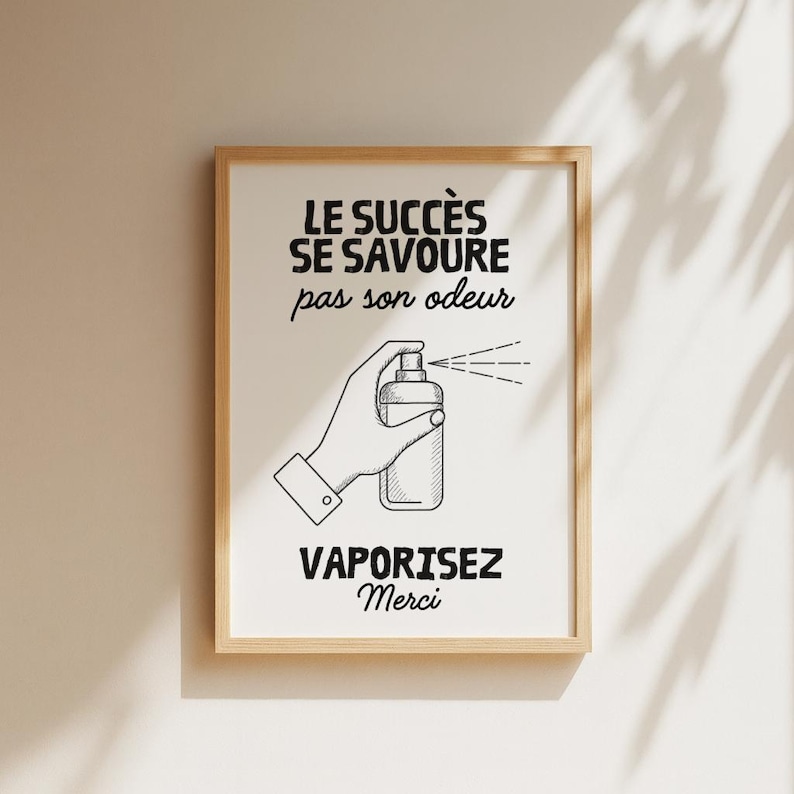 K&ouml;nnte beinhalten: Ein gerahmter Druck mit wei&szlig;em Hintergrund und schwarzem Text. Der Text lautet "LE SUCC&Egrave;S SE SAVOURE pas son odeur" und "VAPORISEZ Merci". Eine Hand wird beim Spr&uuml;hen einer Flasche dargestellt. Der Rahmen ist hellbraun.