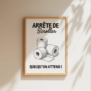 K&ouml;nnte beinhalten: Ein gerahmter Druck mit dem Text "ARR&Ecirc;TE DE Scroller" und "QUELQU'UN ATTEND!" &uuml;ber und unter einer Zeichnung von drei Toilettenpapierrollen. Das Kunstwerk ist in Schwarzwei&szlig; gehalten, mit einem hellbraunen Holzrahmen.