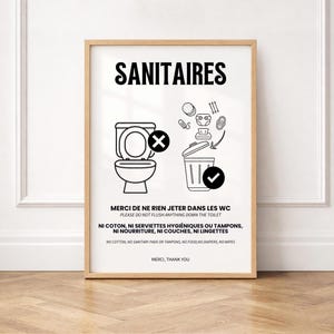 Peut inclure: Une affiche encadrée avec le mot SANITAIRES en haut. Elle présente un graphique noir et blanc d'un WC avec une croix et une poubelle avec une coche, montrant les objets à jeter à la poubelle. Le texte indique de ne rien jeter dans les WC, comme le coton, les serviettes hygiéniques, les tampons, la nourriture, les couches ou les lingettes.