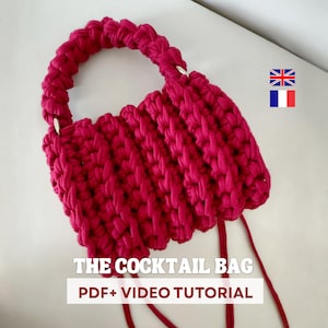 May include: A handmade, magenta-colored crochet bag with a rounded handle and a rectangular body. The bag features the text "THE COCKTAIL BAG PDF+ VIDEO TUTORIAL". The bag is made of thick yarn and has two long, dangling yarn ends.