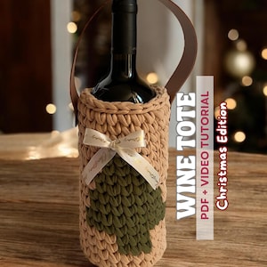 May include: A beige crocheted wine tote with a brown leather handle, holding a wine bottle. The tote features a green tree design and a white ribbon. Text on the side reads "WINE TOTE PDF + VIDEO TUTORIAL Christmas Edition."