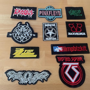 May include: A collection of embroidered patches featuring various band logos. Patches include logos for Exodus, Pink Floyd, Disturbed, Pentagram, Black Veil Brides, ZZ Top, Limp Bizkit, Twisted Sister, AC/DC, and others. The patches are black with colorful embroidered designs.