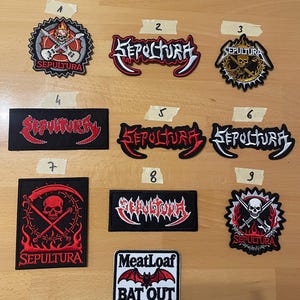 May include: A selection of nine embroidered patches, showcasing band logos and imagery. The patches feature the band name "Sepultura" in different styles, plus a "Meatloaf Bat Out of Hell" design. Predominant colours are red, black, and white.