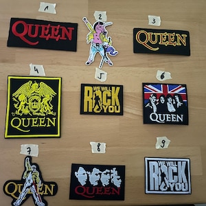 Könnte beinhalten: Eine Sammlung von neun Queen-Patches. Die Patches zeigen den Bandnamen, Albumcover und ikonische Bilder. Farben sind Schwarz, Gold, Rot, Weiß und Blau. Die Patches sind rechteckig und quadratisch.