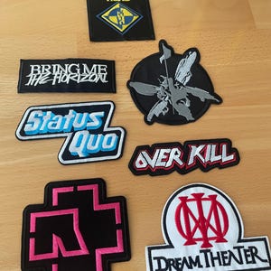 Op de afbeelding: Een verzameling geborduurde patches met verschillende bandlogo's en namen. De patches bevatten "Machine Head", "Bring Me The Horizon", "Status Quo", "Over Kill", een kruisvormig ontwerp en "Dream Theater". De patches zijn in verschillende kleuren, waaronder zwart, wit, blauw en rood.