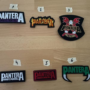 Puede incluir: Colección de seis parches bordados con el nombre de la banda "PANTERA" en varios diseños. Algunos parches incluyen el texto "COWBOYS FROM HELL" y "HELL PATROL". Los parches son de color negro, rojo, naranja y verde.