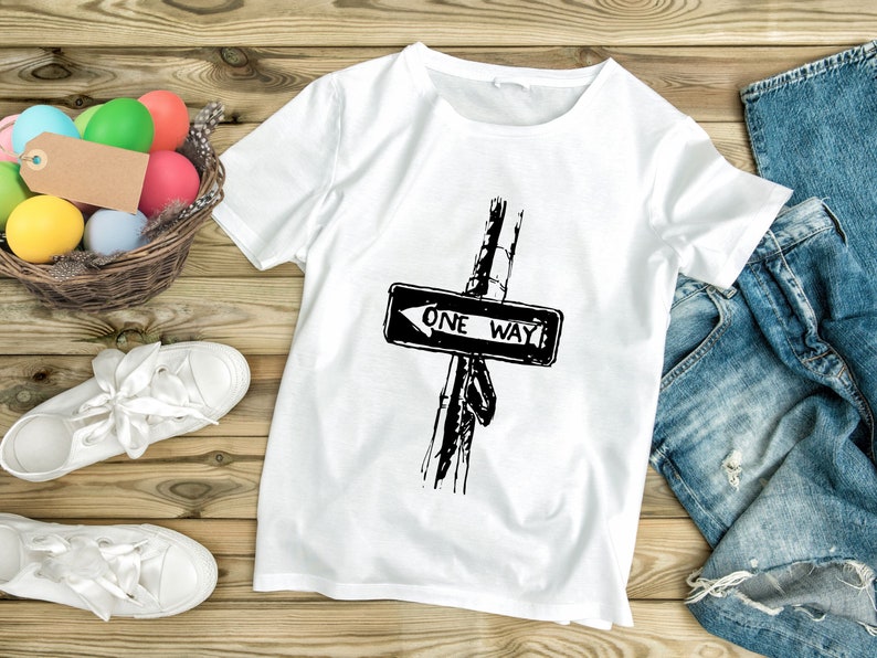 K&ouml;nnte beinhalten: Wei&szlig;es T-Shirt mit einem schwarz-wei&szlig;en "ONE WAY" Stra&szlig;enschild-Motiv. Das Bild zeigt wei&szlig;e Turnschuhe, einen Korb mit bunten Eiern und eine blaue Jeans auf einer Holzoberfl&auml;che.