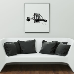 K&ouml;nnte beinhalten: Ein gerahmter Schwarz-Wei&szlig;-Entwurf einer Br&uuml;cke mit der Aufschrift "New York" h&auml;ngt &uuml;ber einem wei&szlig;en Sofa mit schwarzen Kissen. Das Kunstwerk zeigt eine detaillierte Strichzeichnung der Br&uuml;ckenstruktur.