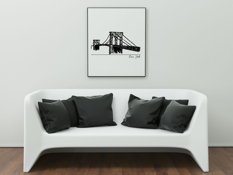 K&ouml;nnte beinhalten: Ein gerahmter Schwarz-Wei&szlig;-Entwurf einer Br&uuml;cke mit der Aufschrift "New York" h&auml;ngt &uuml;ber einem wei&szlig;en Sofa mit schwarzen Kissen. Das Kunstwerk zeigt eine detaillierte Strichzeichnung der Br&uuml;ckenstruktur.