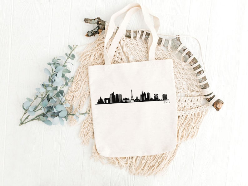 May include: A white canvas tote bag with a black silhouette of the Paris skyline, including the Eiffel Tower, and the word "Paris" printed below.