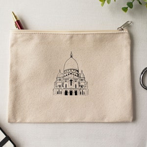 May include: A beige canvas zippered pouch with a black and white illustration of the Sacr&eacute;-C&oelig;ur Basilica in Paris.