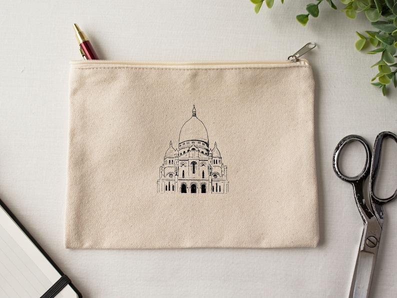 May include: A beige canvas zippered pouch with a black and white illustration of the Sacr&eacute;-C&oelig;ur Basilica in Paris.