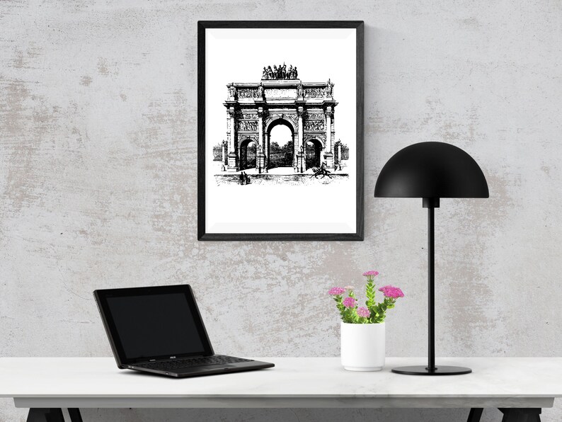 May include: Black and white line art print of an archway with a black frame, a black lamp with a dome-shaped shade, a laptop computer, and a potted plant with pink flowers on a white table.