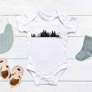 May include: White baby onesie with a black silhouette of the Shanghai skyline and the word "SHANGHAI" printed below.