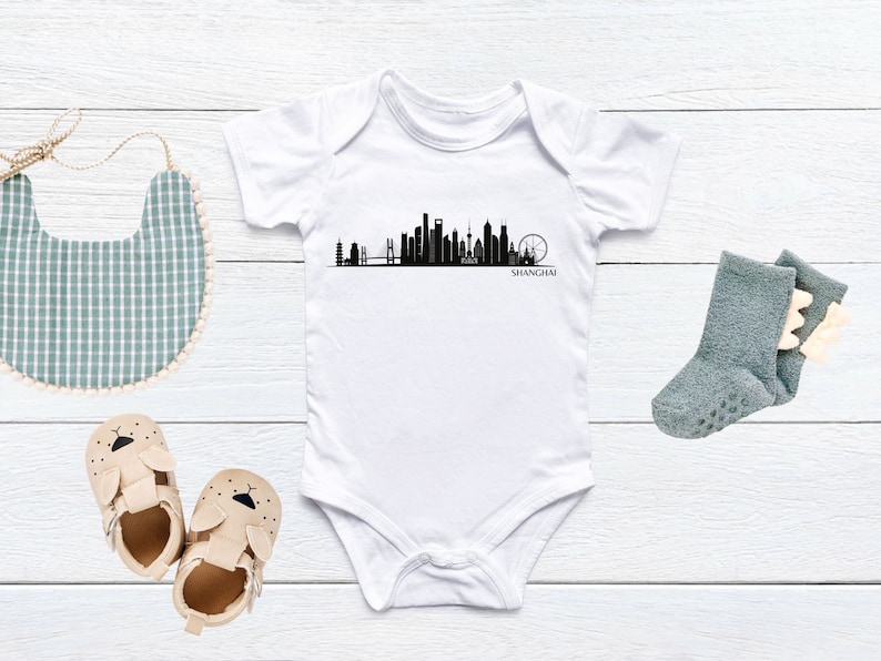 May include: White baby onesie with a black silhouette of the Shanghai skyline and the word "SHANGHAI" printed below.