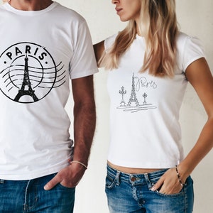 May include: Two white t-shirts with a black Eiffel Tower design. One shirt has the word "PARIS" in a circle around the tower. The other shirt has a more minimalist design with the word "Paris" written in cursive.