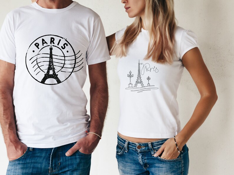 May include: Two white t-shirts with a black Eiffel Tower design. One shirt has the word "PARIS" in a circle around the tower. The other shirt has a more minimalist design with the word "Paris" written in cursive.