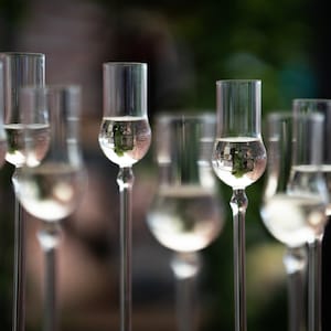 May include: A group of clear glass shot glasses filled with a clear liquid. The liquid reflects the surrounding environment, creating a blurry image of the background.