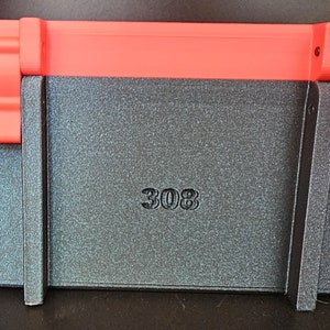 May include: A black and red storage case with the number "308" embossed on the front. The case has a textured surface and a red lid and clasps. The case is designed to protect the contents inside.