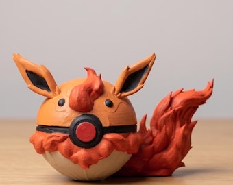 May include: A handcrafted orange and cream-colored sculpture of a cartoon character with large ears and a fiery tail. The character has a round body with black and red accents, and is posed on a wooden surface.