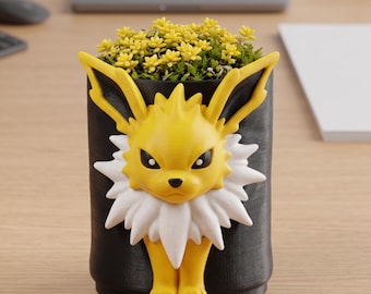 May include: A black planter featuring a yellow and white Jolteon design. The planter is filled with small yellow flowers. The Jolteon has yellow ears, a white collar, and yellow feet. The planter is on a wooden desk.