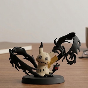 Puede incluir: Una figura de Mimikyu, con un cuerpo color crema, una cara cosida y una cola negra y dentada. La figura está sobre una base negra, con un detalle de garra roja. Probablemente sea un artículo de colección.