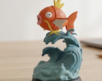 May include: A detailed figurine of a cartoon fish, orange with yellow and white accents, atop stylized blue waves. The fish has a surprised expression. The base is black, and the figurine is set on a light-colored surface.