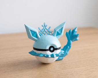 May include: A light blue and white figurine with a black circular detail. The figurine has large, pointed ears, a crown-like structure, and a tail. The figurine is on a wooden surface.