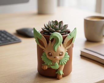 May include: A brown ceramic planter featuring a cartoon character design with green accents, holding a succulent plant. The planter has a detailed face and leaf-like features. The succulent has green and reddish-brown leaves.