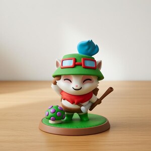 May include: A figurine of a cartoon character with a green hat, red goggles, and a red scarf. The character is holding a wooden stick and standing on a green base with a mushroom. The figurine is on a wooden surface.