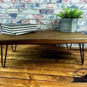 May include: A dark brown wooden coffee table with a rectangular top and hairpin legs. The table is sitting on a wooden floor.
