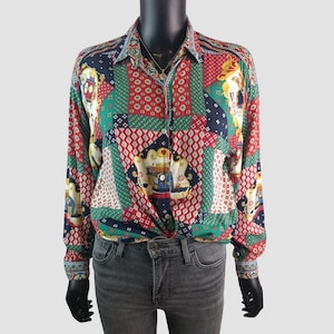 Könnte beinhalten: Ein langärmliges Button-Down-Hemd mit einem Patchwork-Design in Rot, Grün, Blau und Weiß. Das Hemd hat einen Kragen und ist an der Taille geknotet. Das Muster umfasst geometrische Formen und dekorative Motive.