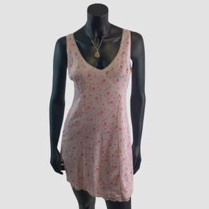 May include: A light pink slip dress with a floral pattern of small pink roses. The dress has a V-neckline trimmed with lace and a matching lace hem. A silver necklace with a pendant is also visible.