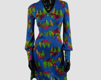 May include: A blue vintage dress with a floral pattern in pink, green, and yellow. The dress has long sleeves and a V-neck. The dress is displayed on a black mannequin.